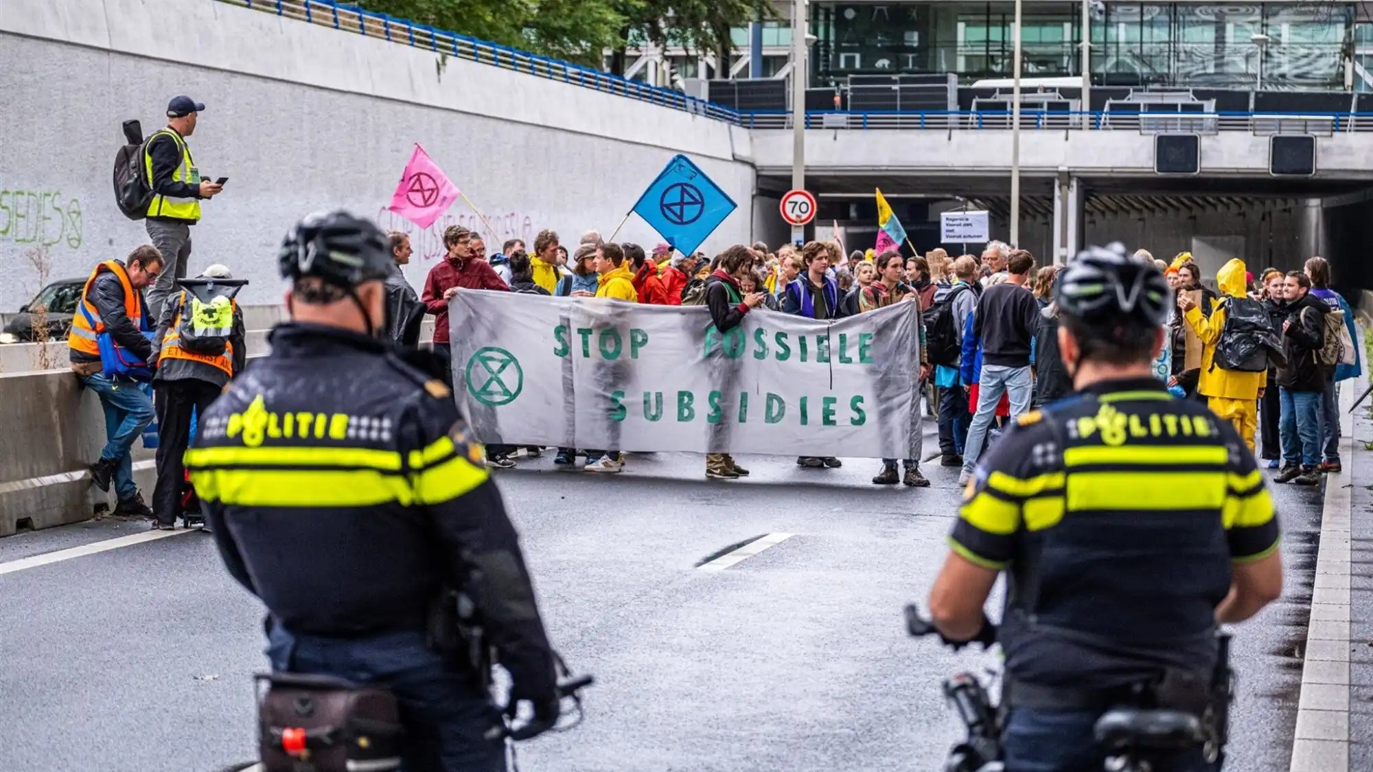 Protesteerders met spandoeken over staal-subsidies terwijl politieagenten op fietsen de demonstratie in de gaten houden.