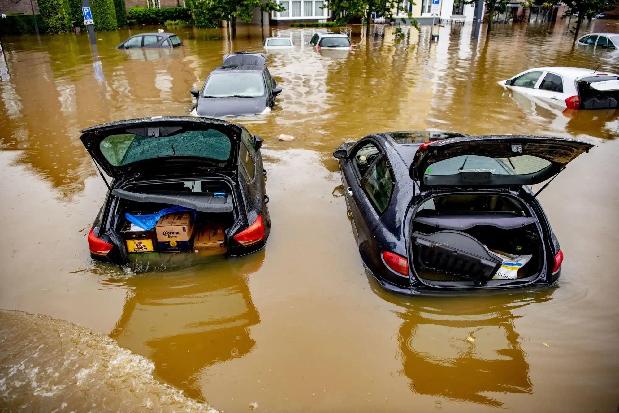 Twee gedeeltelijk ondergedompelde auto's met open koffers in het overstromingswater.